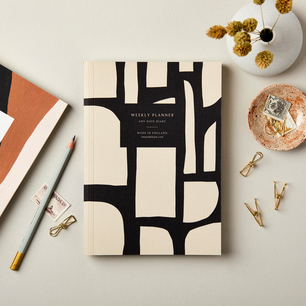Weekly Planner,  A5, Undated with 'Any Date Diary' text, abstract black/cream design, on cream backdrop with vase and stationery.